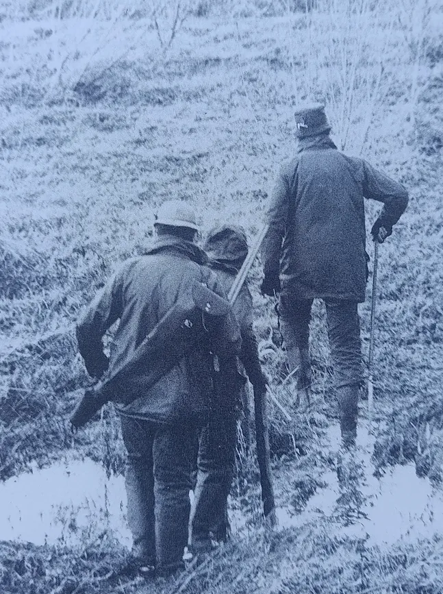 Two people with guns walking on a hillside.